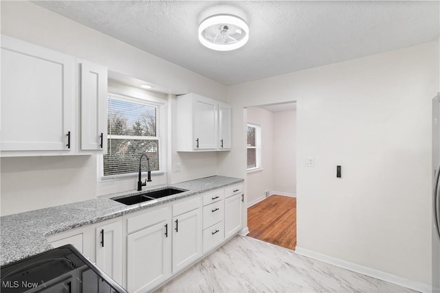 kitchen featuring white cabinets, light stone counters, sink, and a textured ceiling