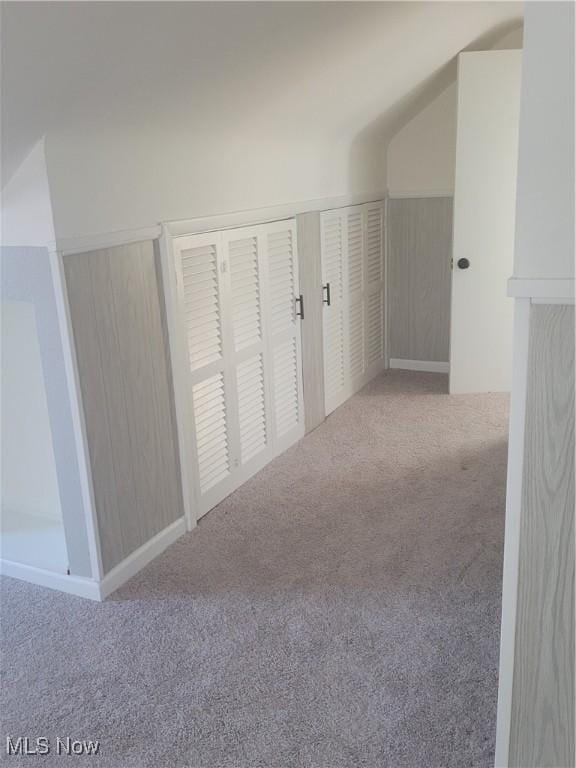 hall with light colored carpet, lofted ceiling, and wood walls