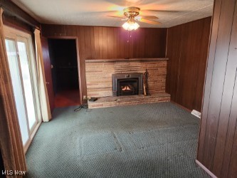 unfurnished living room featuring carpet flooring, ceiling fan, and wooden walls