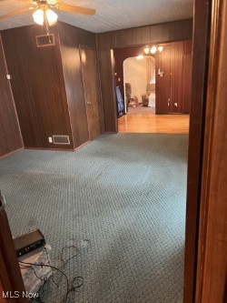 carpeted empty room with ceiling fan and wood walls