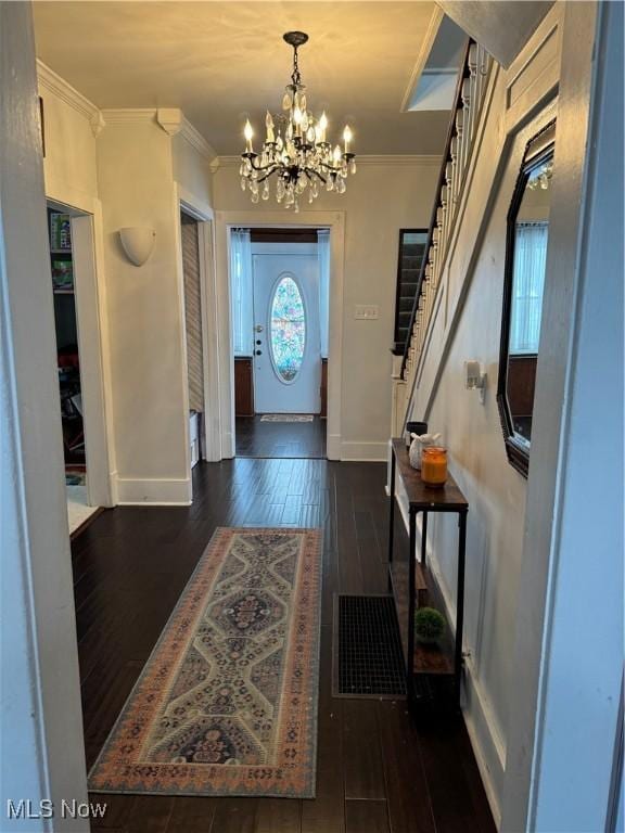 foyer entrance featuring dark hardwood / wood-style flooring, ornamental molding, and an inviting chandelier