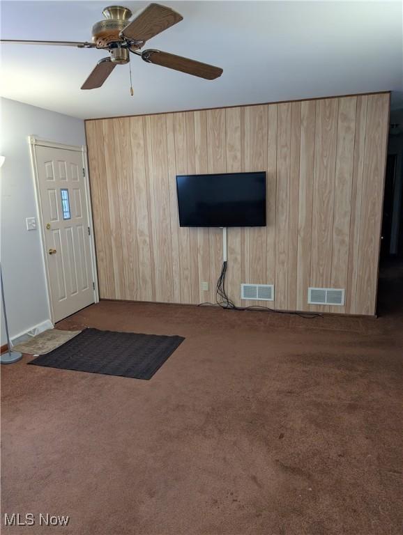 entryway with carpet floors, ceiling fan, and wood walls