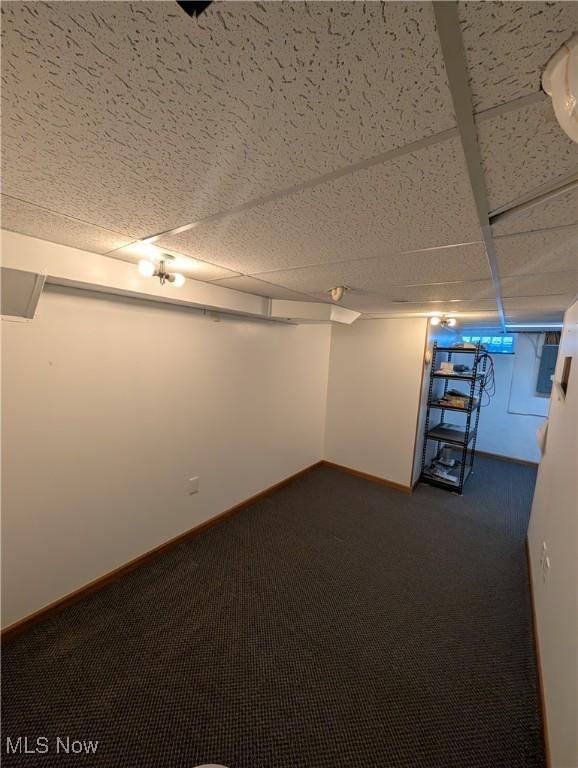 basement with a paneled ceiling and dark carpet