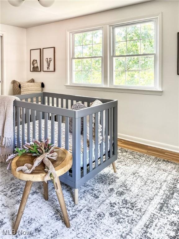 bedroom with ceiling fan, a nursery area, and wood-type flooring