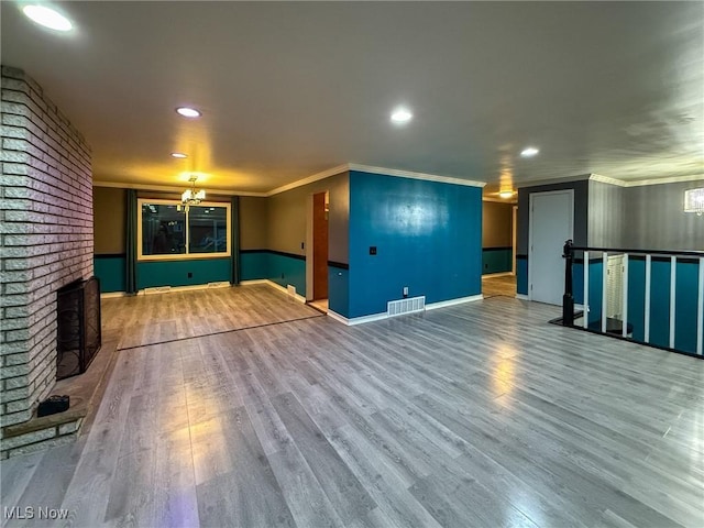 unfurnished living room with a chandelier, hardwood / wood-style floors, a brick fireplace, and ornamental molding