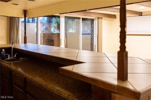 bar featuring tile countertops, dark brown cabinets, and sink