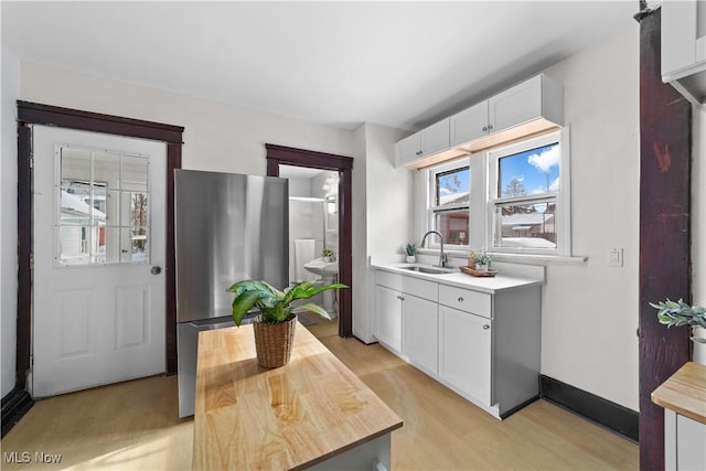 kitchen featuring stainless steel fridge, light hardwood / wood-style flooring, white cabinetry, and sink