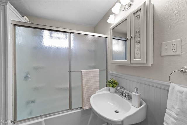 bathroom with sink and bath / shower combo with glass door