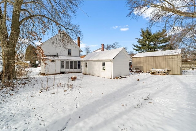 snow covered rear of property featuring an outdoor structure