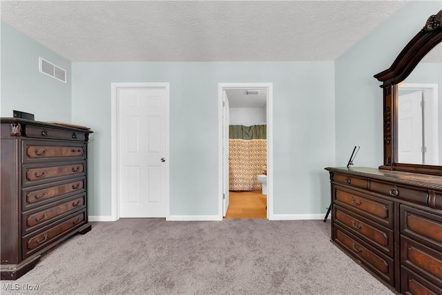 carpeted bedroom featuring ensuite bathroom and a textured ceiling