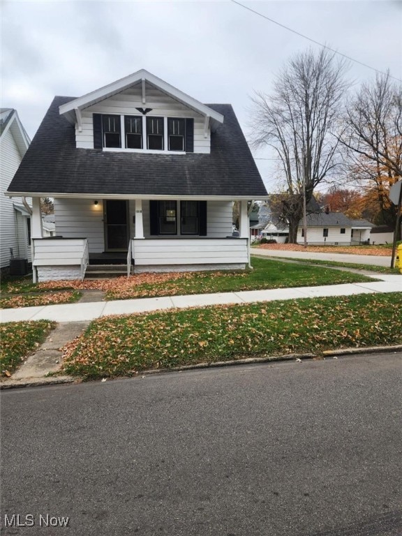 view of front facade featuring covered porch, central air condition unit, and a front yard