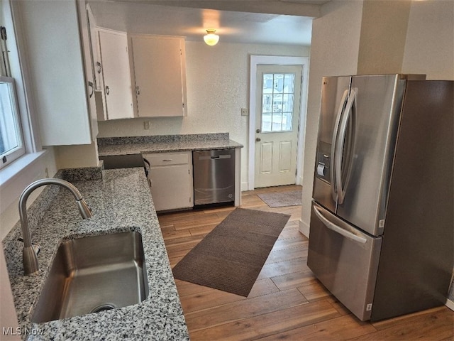 kitchen featuring light stone countertops, appliances with stainless steel finishes, light wood-type flooring, sink, and white cabinets