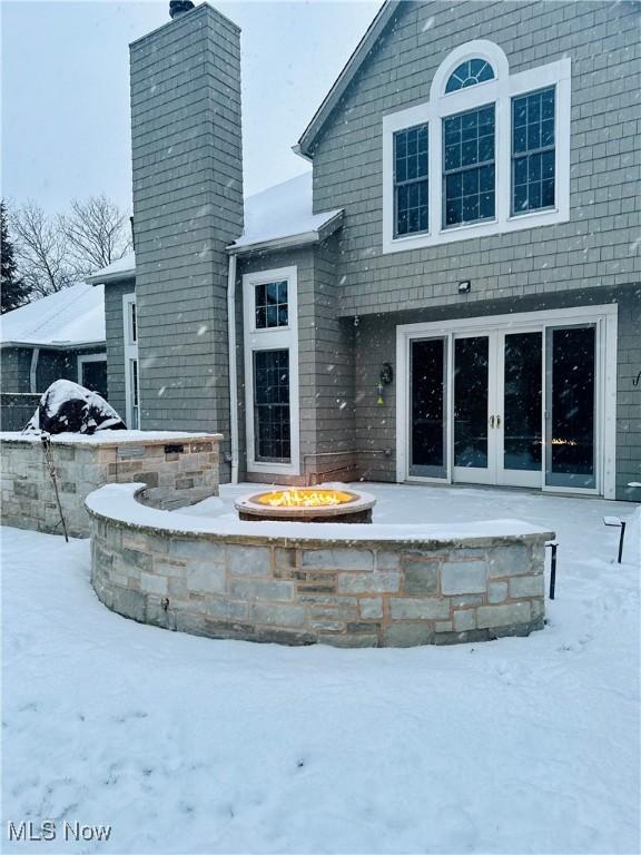 snow covered back of property with french doors and an outdoor fire pit