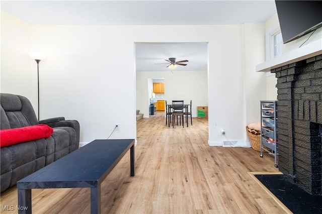 living room featuring ceiling fan, light hardwood / wood-style floors, and a brick fireplace