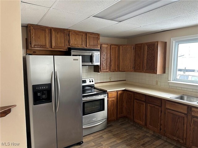 kitchen featuring a paneled ceiling, sink, tasteful backsplash, dark hardwood / wood-style flooring, and stainless steel appliances