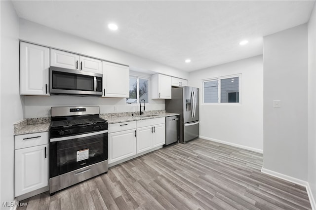 kitchen with appliances with stainless steel finishes, light stone counters, white cabinetry, and sink