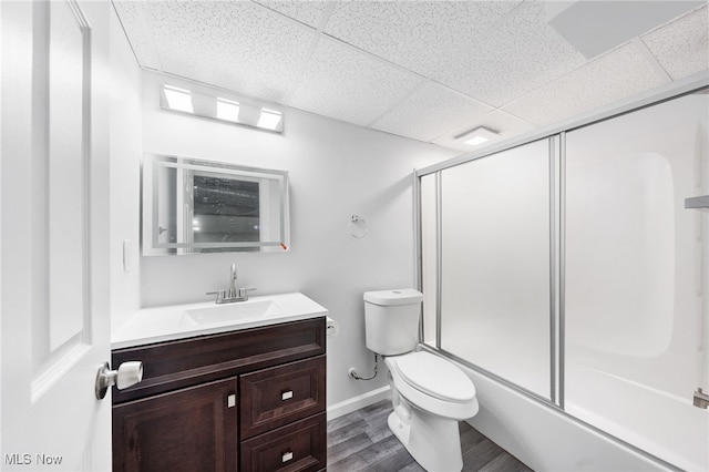 full bathroom featuring wood-type flooring, combined bath / shower with glass door, a paneled ceiling, toilet, and vanity