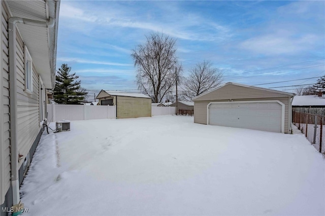 snowy yard featuring an outbuilding, a fenced backyard, a detached garage, and cooling unit