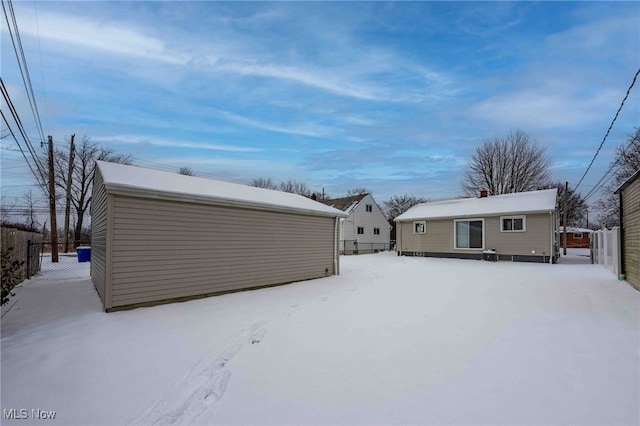 snow covered house featuring an outbuilding and fence