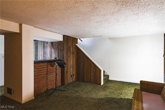 basement featuring carpet flooring, wood walls, and a textured ceiling