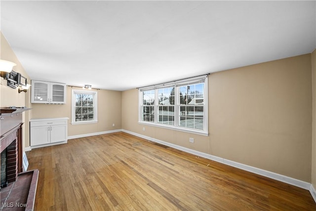 unfurnished living room with light wood-type flooring and a brick fireplace