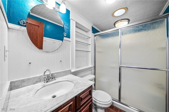 bathroom with vanity, a shower with door, crown molding, toilet, and wood walls