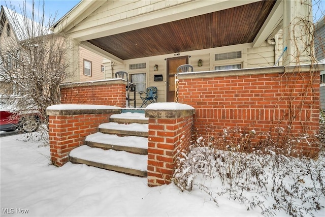 snow covered property entrance with covered porch