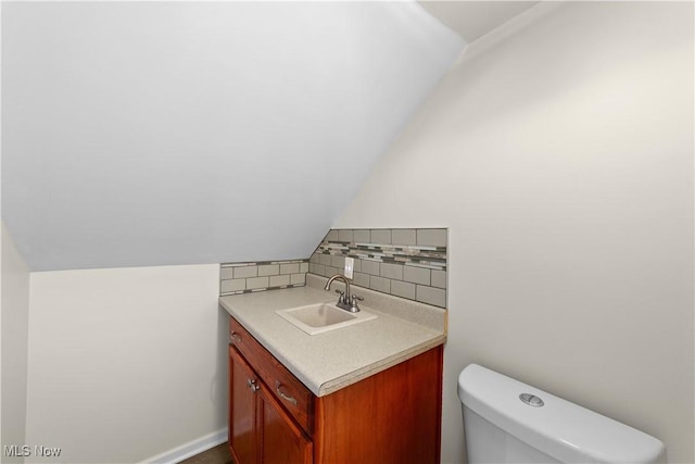 bathroom featuring decorative backsplash, toilet, vanity, and vaulted ceiling