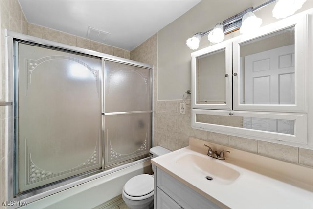 full bathroom featuring vanity, combined bath / shower with glass door, tile walls, and toilet