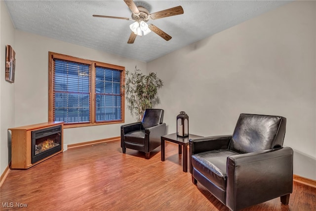 living area featuring ceiling fan, a textured ceiling, and light hardwood / wood-style flooring