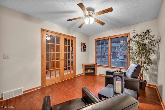 living area with ceiling fan, french doors, hardwood / wood-style floors, and a textured ceiling