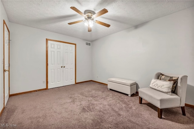 living area with ceiling fan, carpet floors, and a textured ceiling