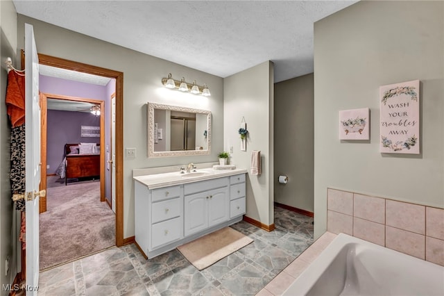 bathroom with ceiling fan, a washtub, vanity, and a textured ceiling