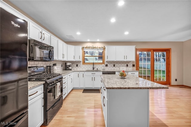 kitchen with black appliances, sink, light stone countertops, a kitchen island, and white cabinetry