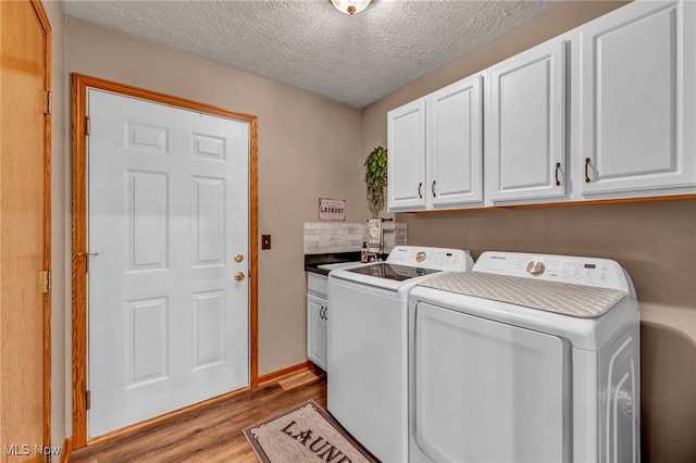 laundry area with washer and clothes dryer, cabinets, sink, light hardwood / wood-style flooring, and a textured ceiling