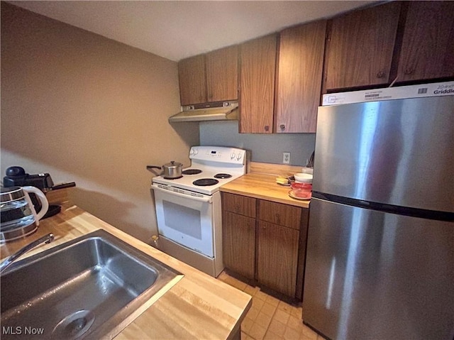 kitchen featuring electric range, butcher block counters, sink, and stainless steel refrigerator