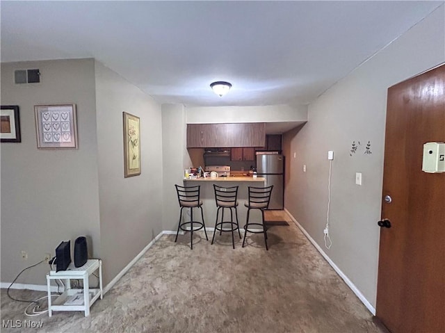 kitchen with kitchen peninsula, stainless steel fridge, light carpet, a kitchen breakfast bar, and exhaust hood