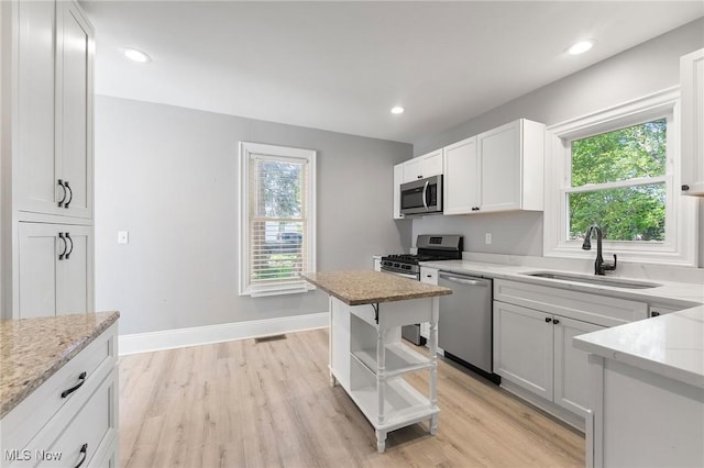 kitchen featuring white cabinets, sink, light hardwood / wood-style flooring, light stone counters, and stainless steel appliances