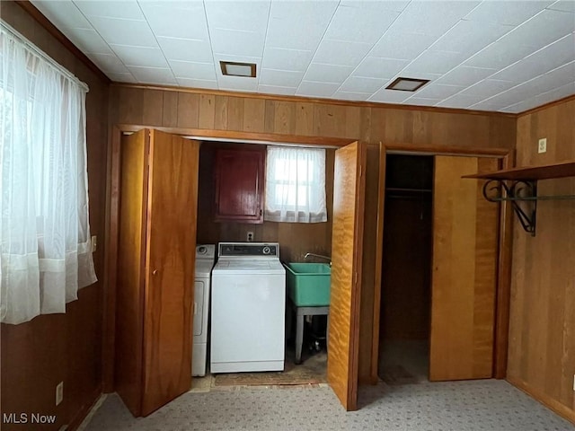 clothes washing area featuring washer and dryer, wooden walls, sink, and cabinets