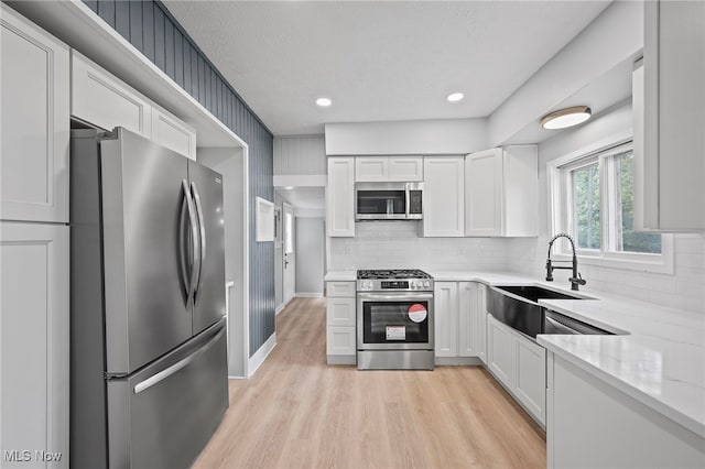 kitchen featuring sink, light stone countertops, appliances with stainless steel finishes, light hardwood / wood-style floors, and white cabinetry