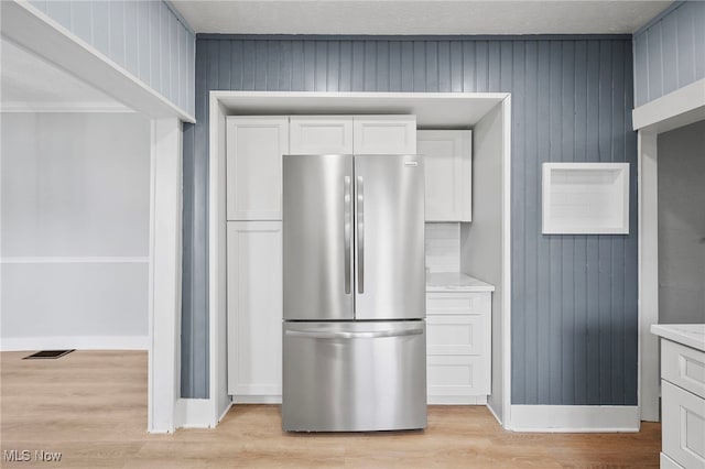 kitchen with white cabinets, stainless steel fridge, light hardwood / wood-style floors, and light stone countertops