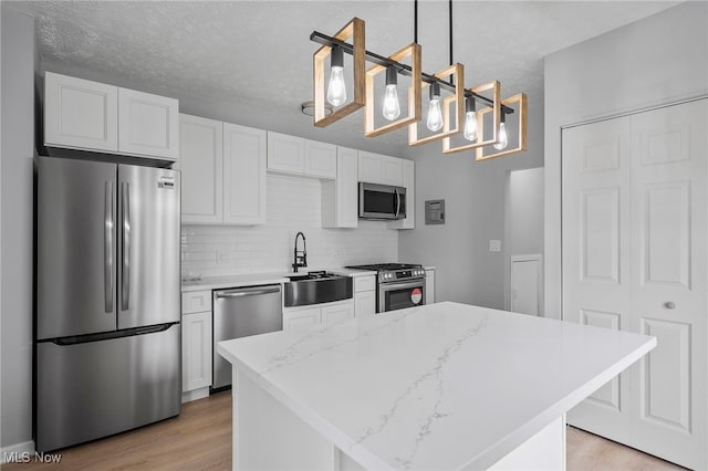 kitchen with sink, white cabinets, decorative light fixtures, and appliances with stainless steel finishes