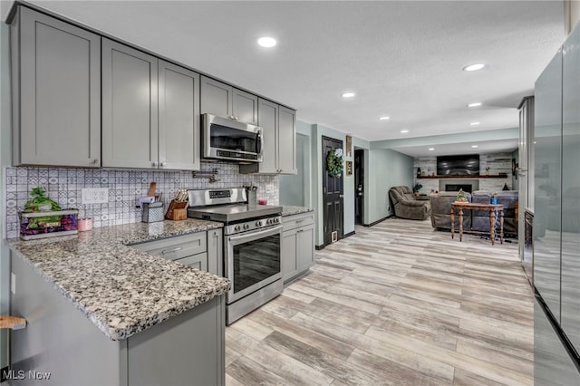 kitchen with gray cabinetry, light stone counters, light hardwood / wood-style flooring, kitchen peninsula, and appliances with stainless steel finishes