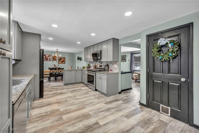 kitchen featuring gray cabinetry, light stone countertops, pendant lighting, appliances with stainless steel finishes, and light wood-type flooring