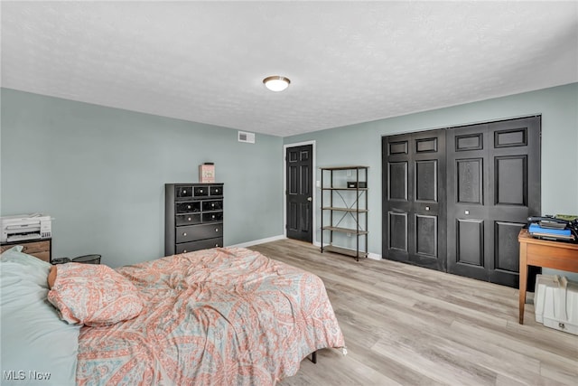 bedroom with a closet, a textured ceiling, and light wood-type flooring