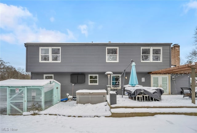 snow covered back of property with a pergola and a hot tub