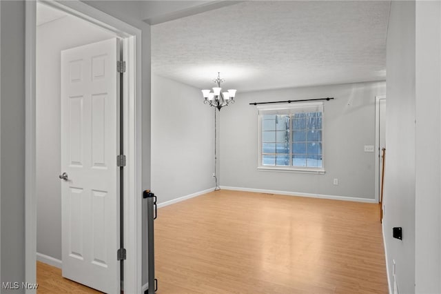 unfurnished room featuring an inviting chandelier, a textured ceiling, and light hardwood / wood-style flooring