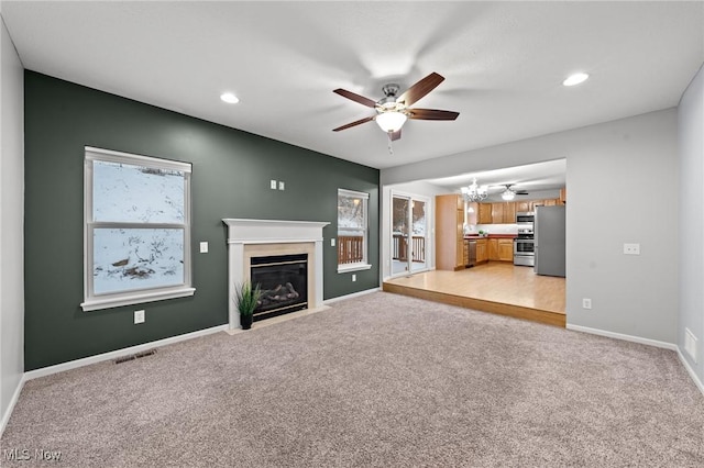 unfurnished living room featuring light colored carpet and ceiling fan with notable chandelier