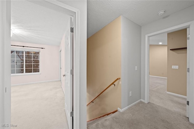 hall featuring light colored carpet and a textured ceiling