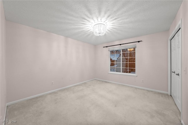 unfurnished room with light carpet, a chandelier, and a textured ceiling